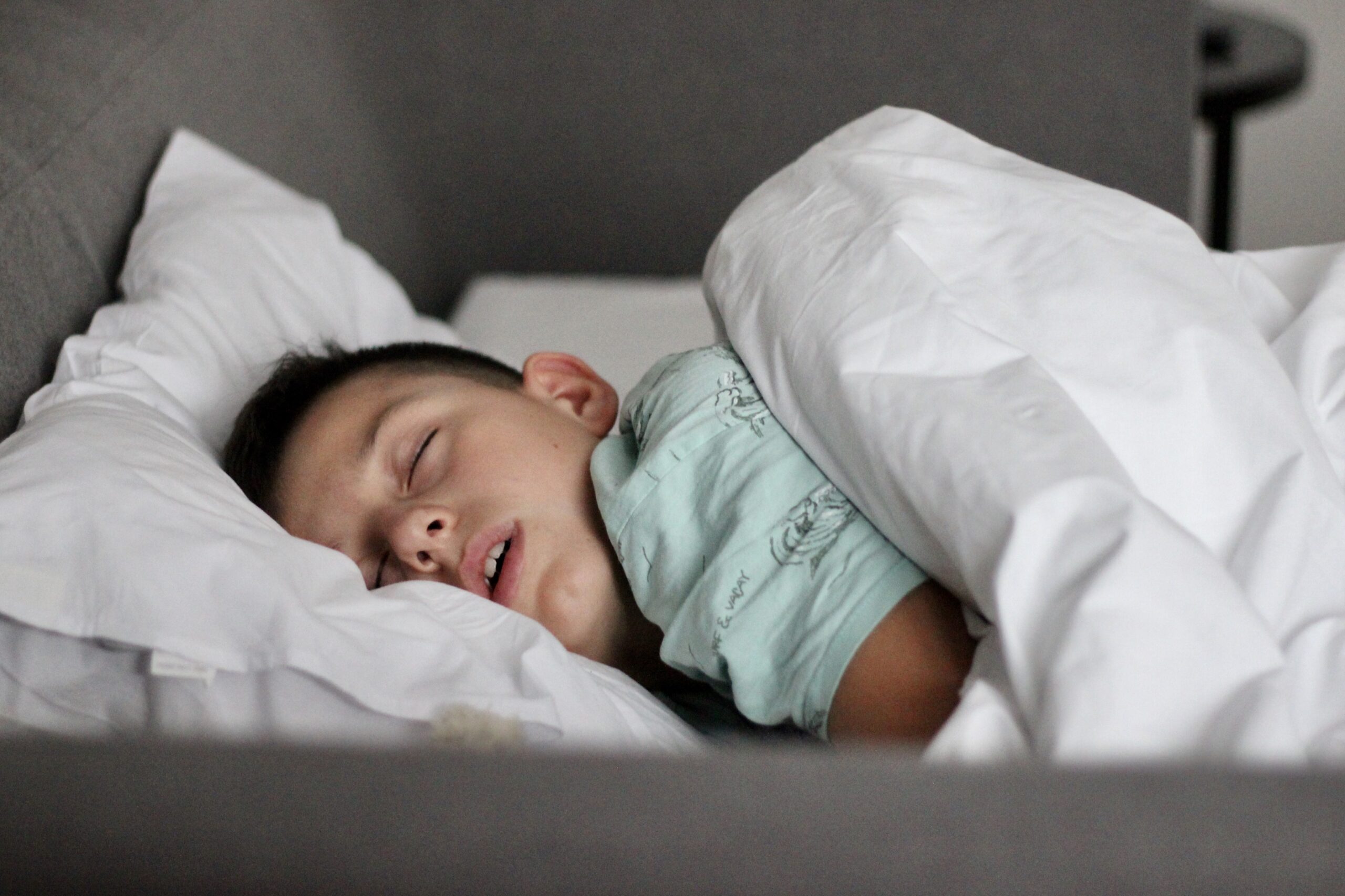 Young child sleeping peacefully in a bed, tucked under white blankets.